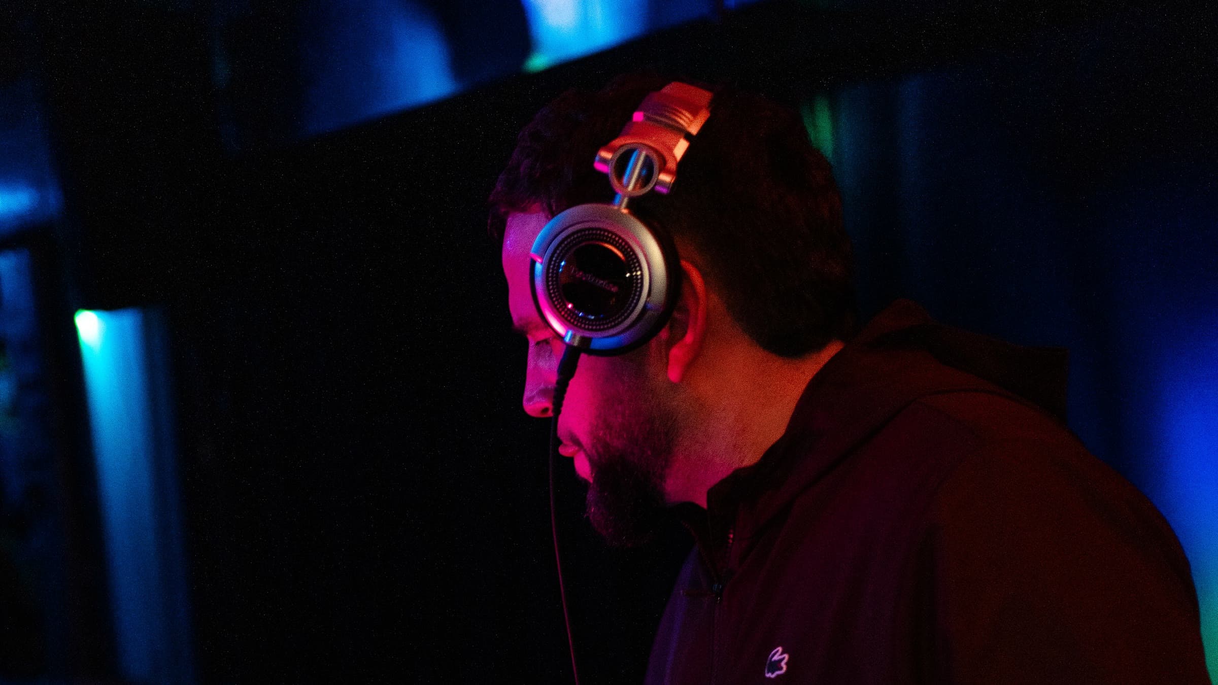 DJ Sergjio mit Kopfhörern im Profil, in rotem und blauem Clublicht