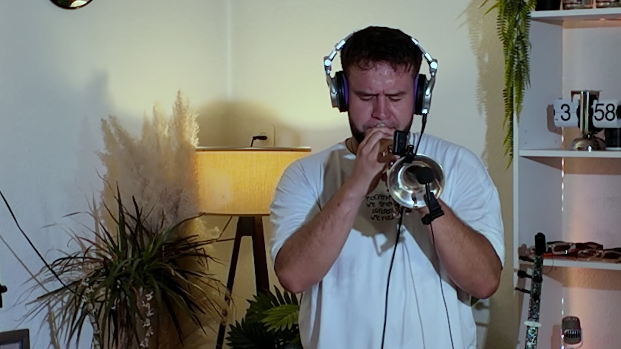 Sergjio spielt mit Kopfhörern Cornet, hinter ihm eine Stehlampe und Pflanzen