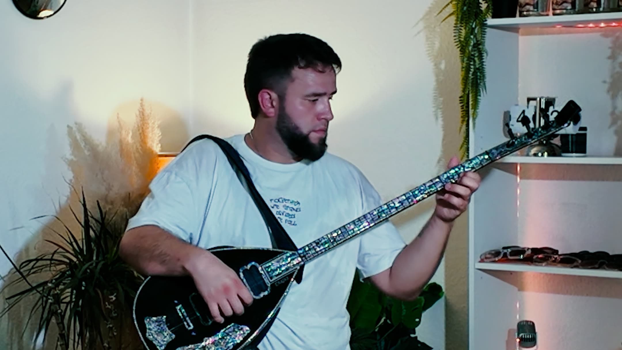 Sergjio spielt die Elektro-Saz, hinter ihm Pflanzen und ein Regal